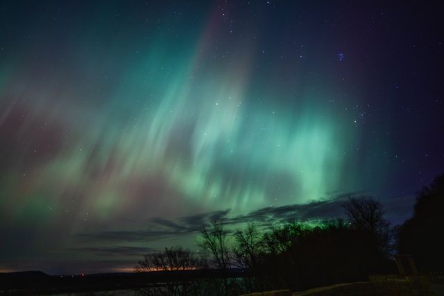 Aurora boreal verde parcialmente cubierta por nubes sobre un paisaje oscuro