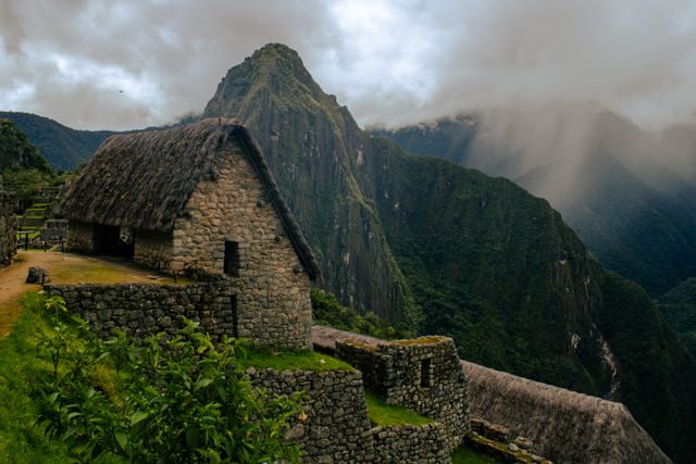 Construcción de piedra con techo de paja en Machu Picchu y Huayna Picchu entre nubes al fondo