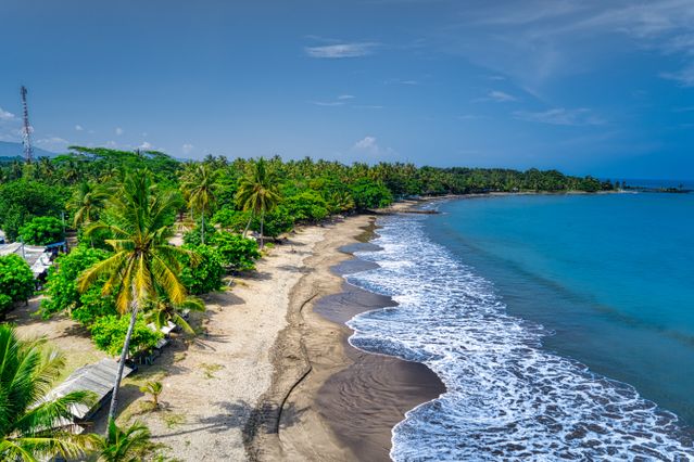 Destinos subestimados del mundo para viajar en 2026 Playa tropical poco concurrida con palmeras, vegetación exuberante y mar azul