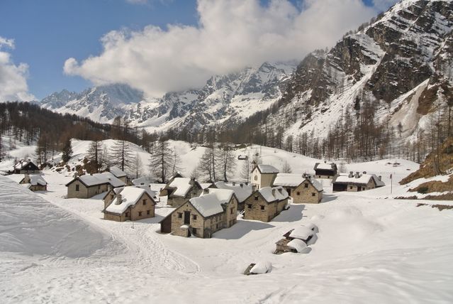 Pueblo de montaña en Italia cubierto de nieve con cumbres alpinas al fondo