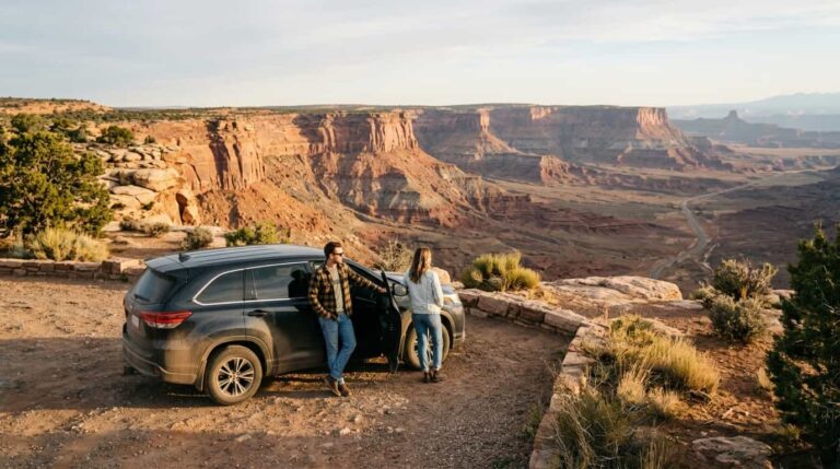 Pareja junto a un auto en un mirador de un paisaje de cañones del suroeste de Estados Unidos
